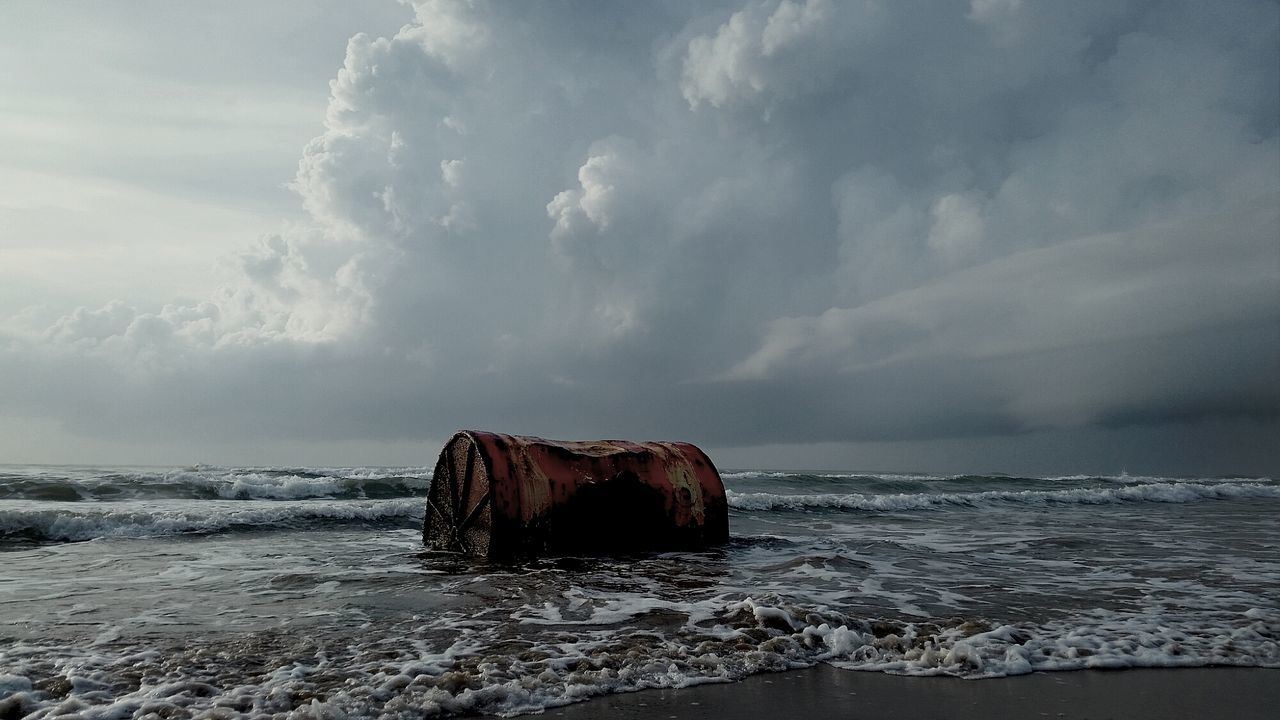 Damaged container on beach against cloudy sky