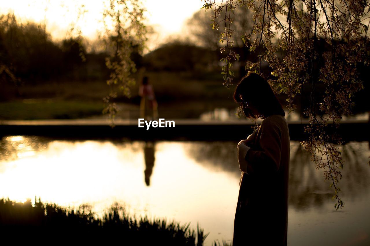 Side view of silhouette woman standing by lake during sunset