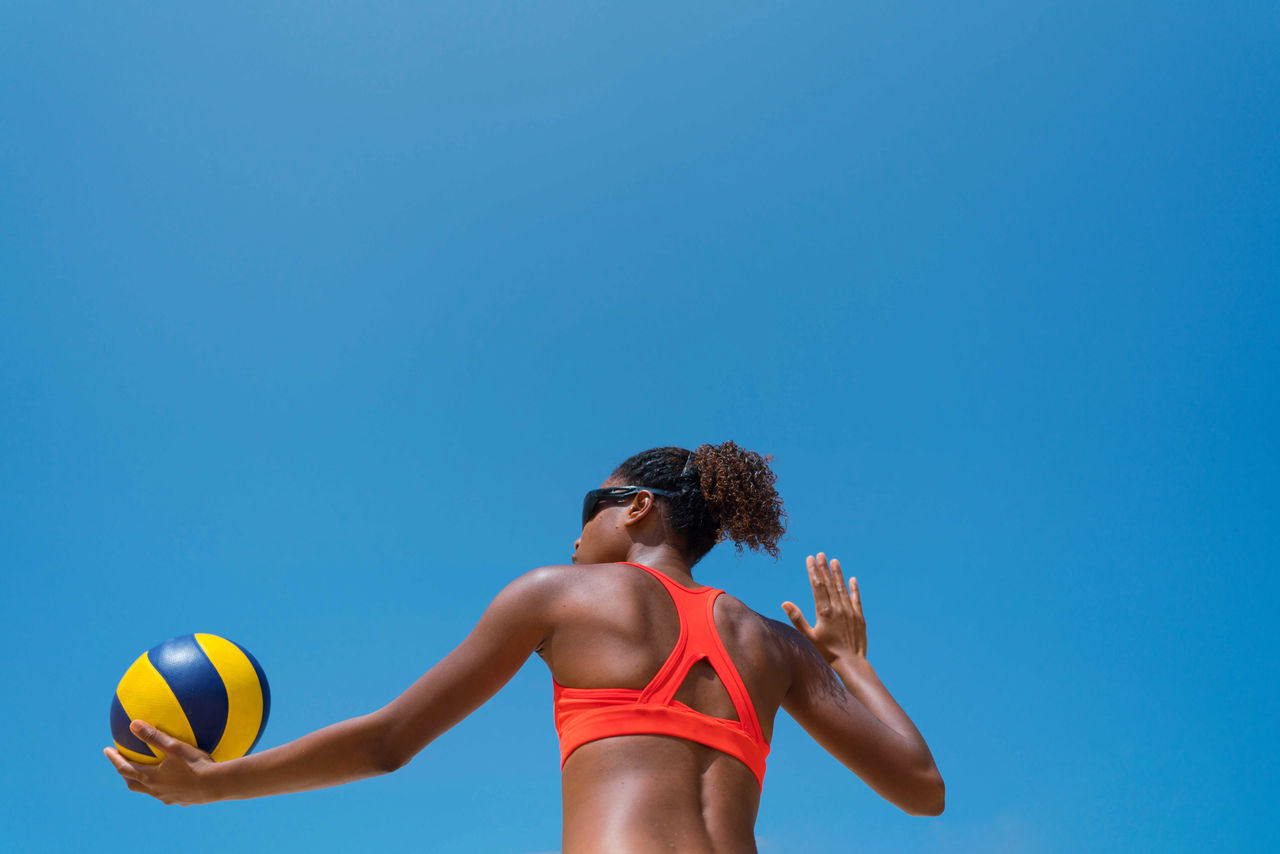 sports, blue, volleyball, one person, clothing, ball, adult, copy space, athlete, young adult, lifestyles, clear sky, sports clothing, competition, motion, sky, women, exercising, person, nature, leisure activity, sports equipment, day, determination, sunny, beach volleyball, net sports, waist up, player, concentration, vitality, outdoors, activity, low angle view, football