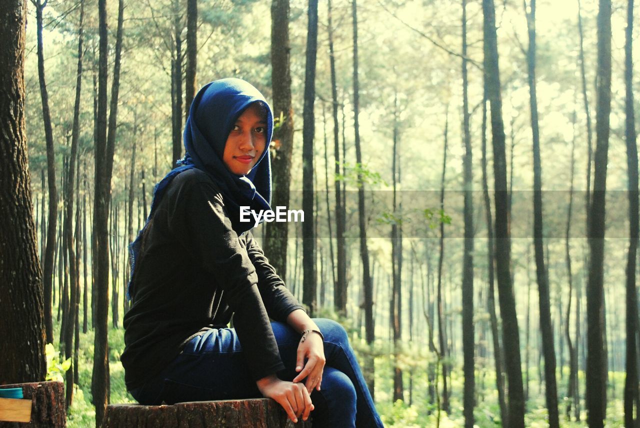 Portrait of woman in hijab sitting on tree stump in forest