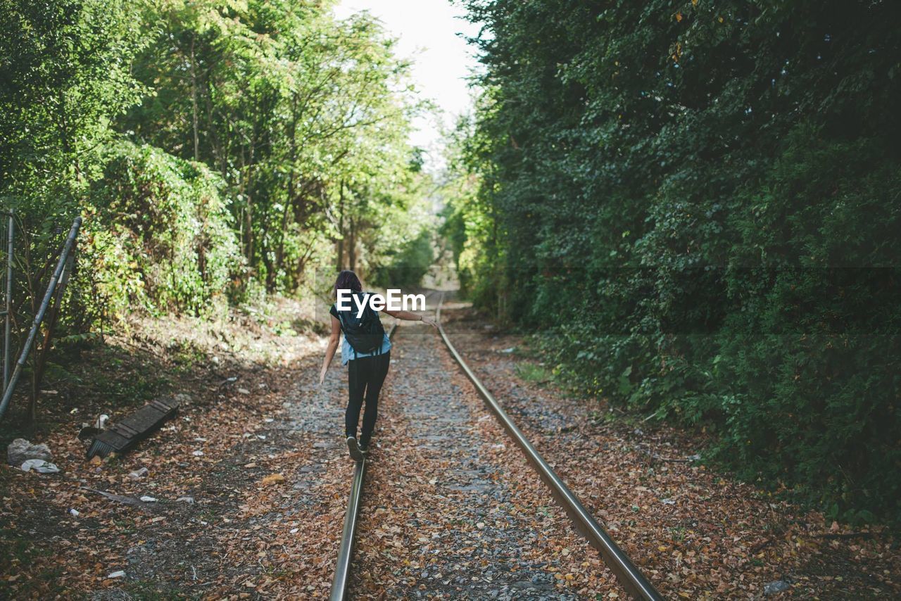 Woman walking on railroad track amidst trees