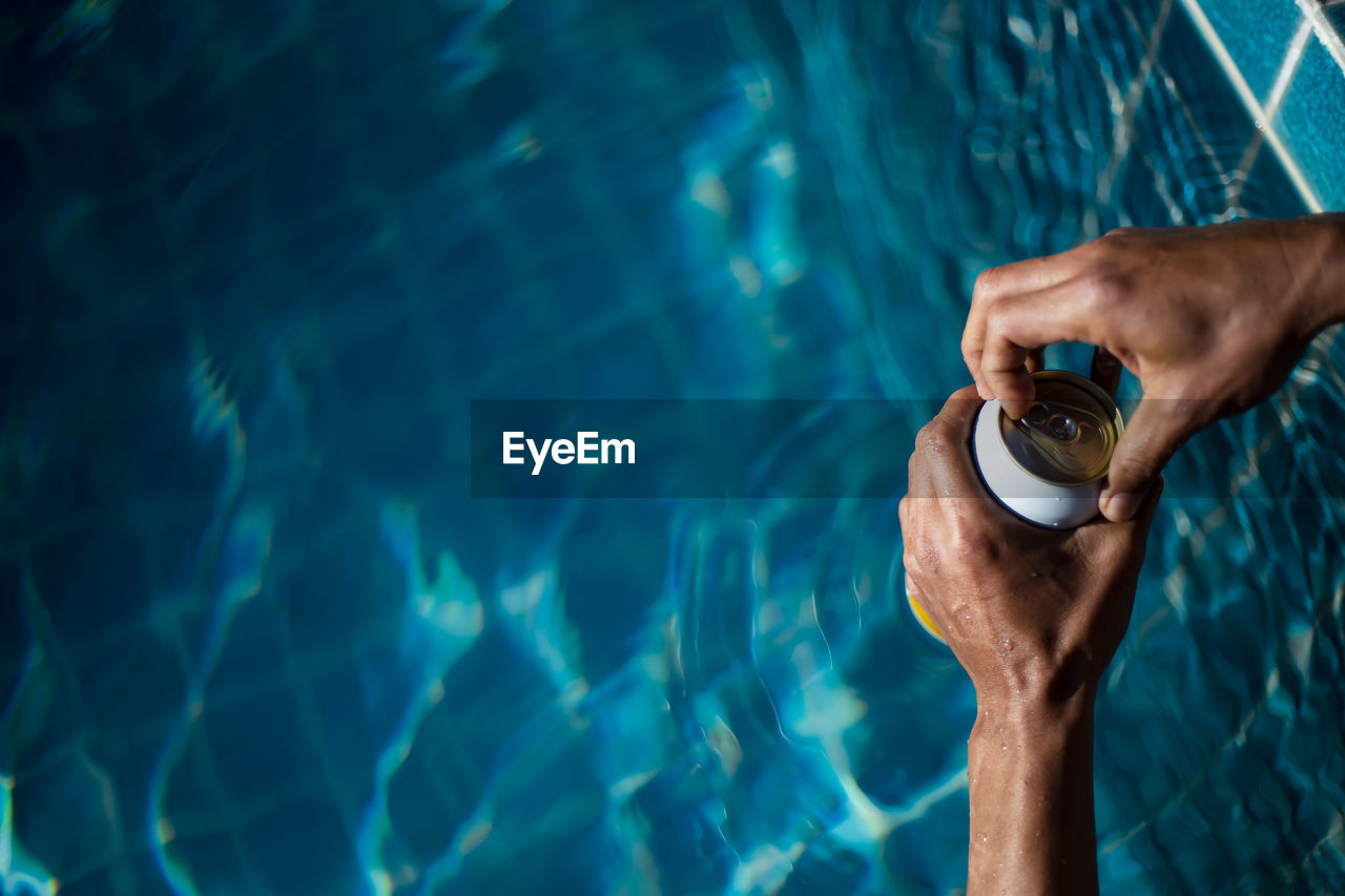 Selective focus white beer can in hand. man is soaking in the pool with an open beer 