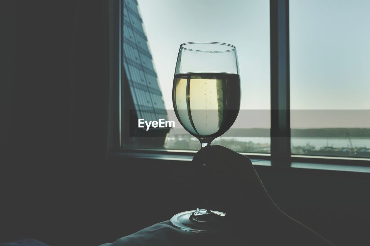 Close-up of hand holding wineglass against window