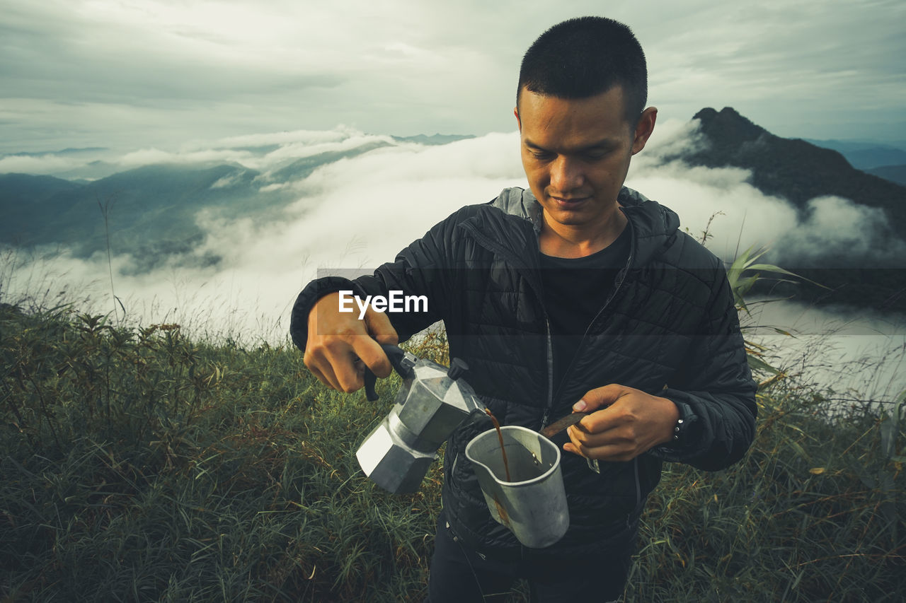 Man pouring black tea in jug while standing on field