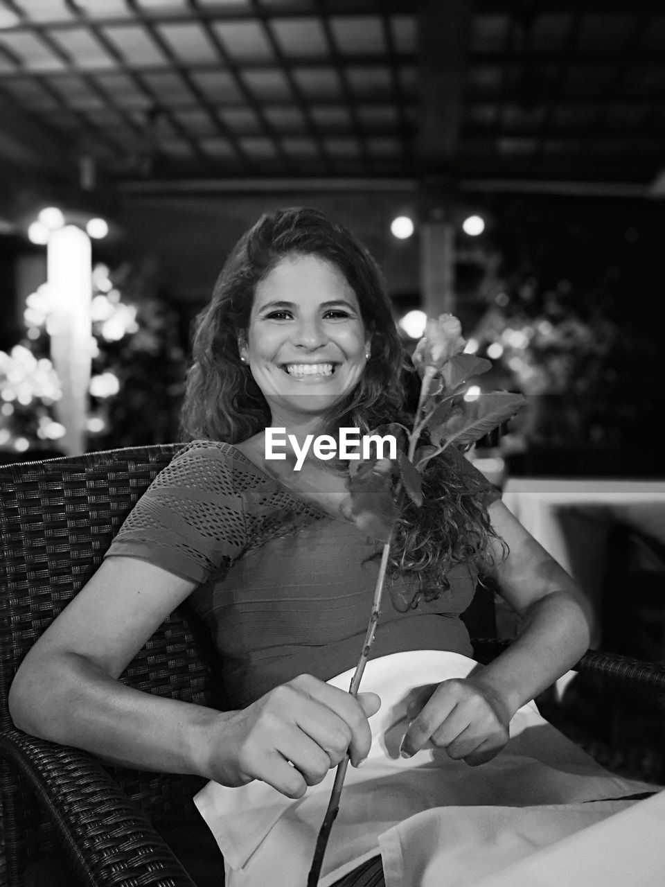 Portrait of smiling woman holding flower while sitting on chair