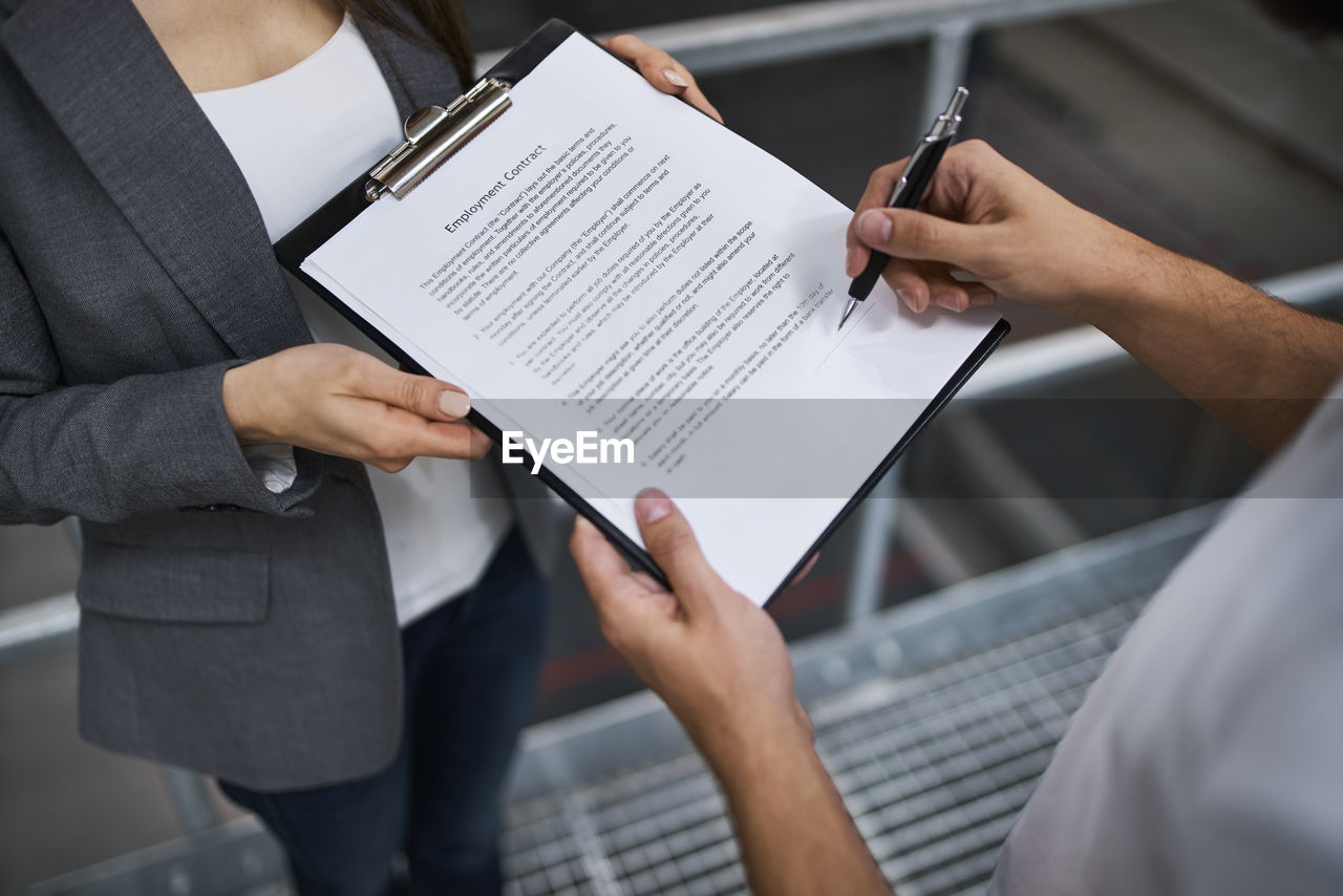 Man signing employment contract in factory held by businesswoman