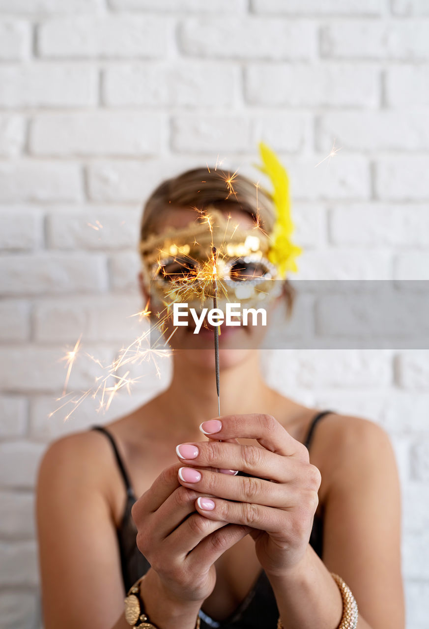 Close-up of woman holding sparkler against wall