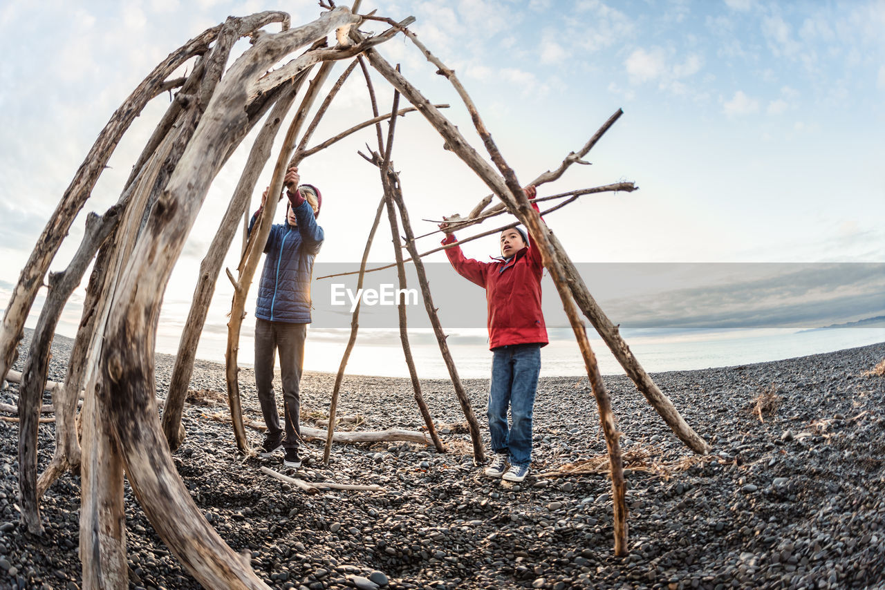 Two brothers building a hut out of driftwood on a rocky beach