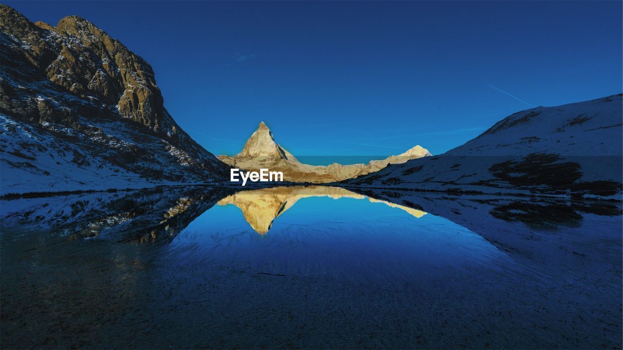 Scenic view of lake and mountains against clear blue sky