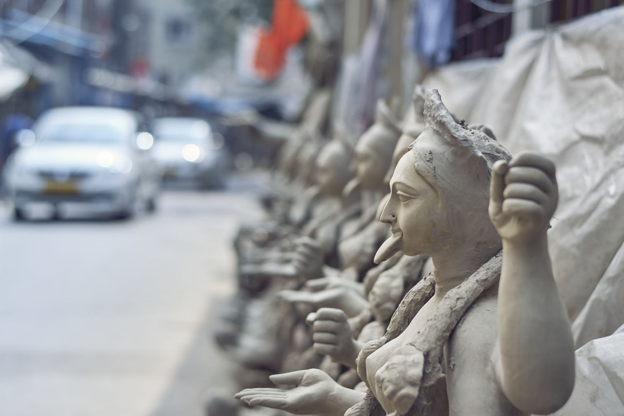 CLOSE-UP OF FEMALE STATUE AGAINST CITY