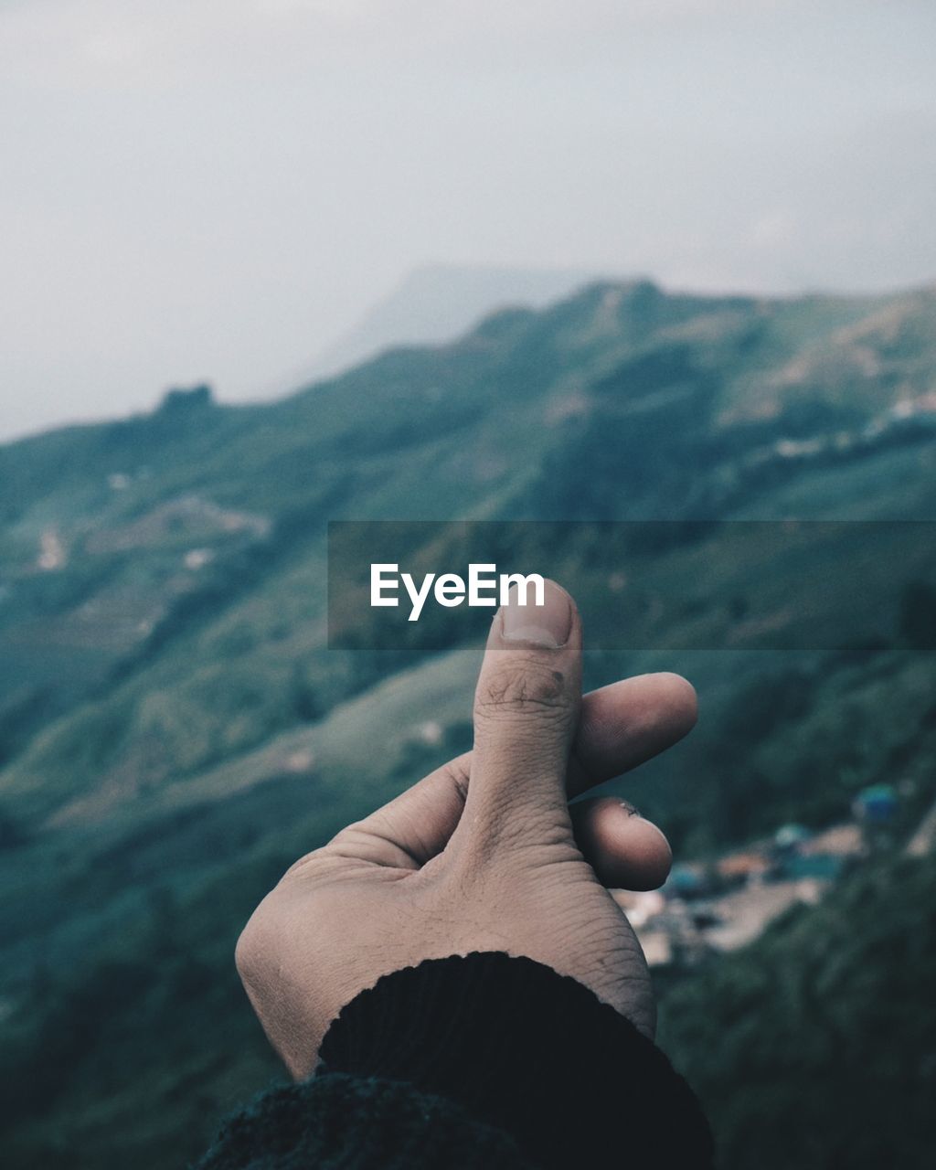 Cropped image of hand snapping fingers against mountains during foggy weather