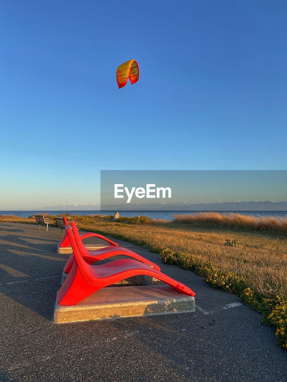 sky, land, nature, toy, flying, transportation, blue, environment, adventure, hot air balloon, windsports, balloon, sports, landscape, clear sky, mid-air, red, scenics - nature, parachute, day, beauty in nature, kite - toy, tranquility, beach, air vehicle, multi colored, kite sports, water, sand, tranquil scene, sea, sunny, horizon, outdoors, leisure activity, kite, travel, wind, sunlight, no people, vehicle, motion, non-urban scene, holiday, extreme sports, travel destinations, vacation, trip, summer