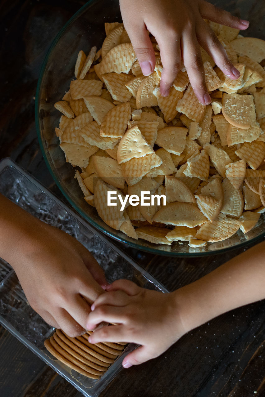 High angle view of hand crushing cookies in the bowl on table. top view.