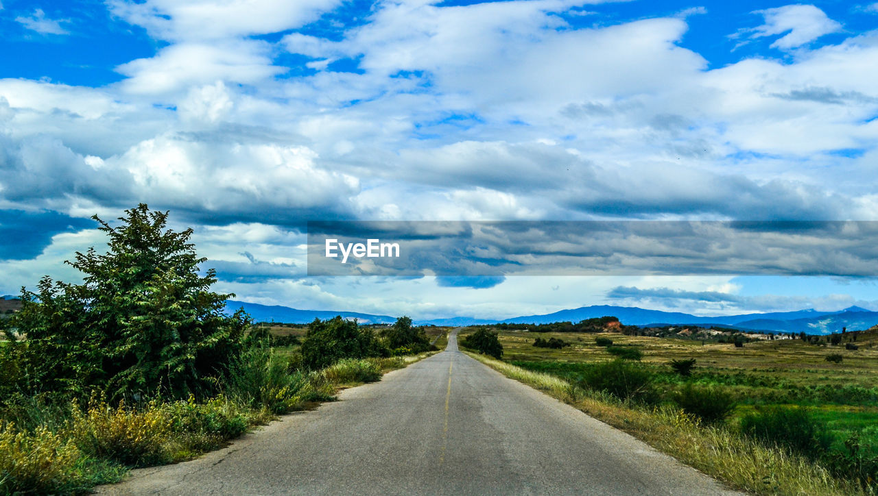 Scenic view of country road against cloudy sky