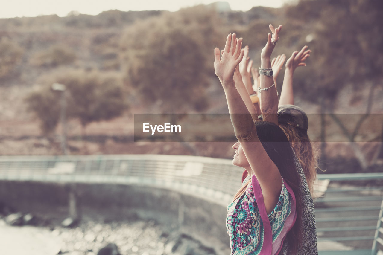 Female friends with arms raised standing at bridge