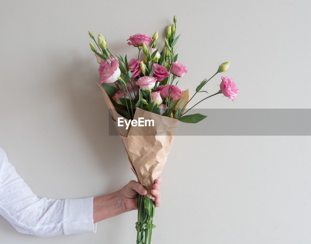 Cropped hand of man holding bouquet against wall