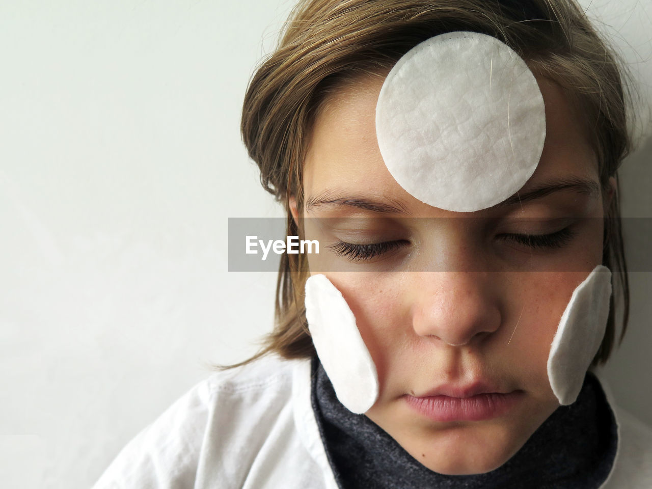 Close-up of girl with cotton pads on face against wall