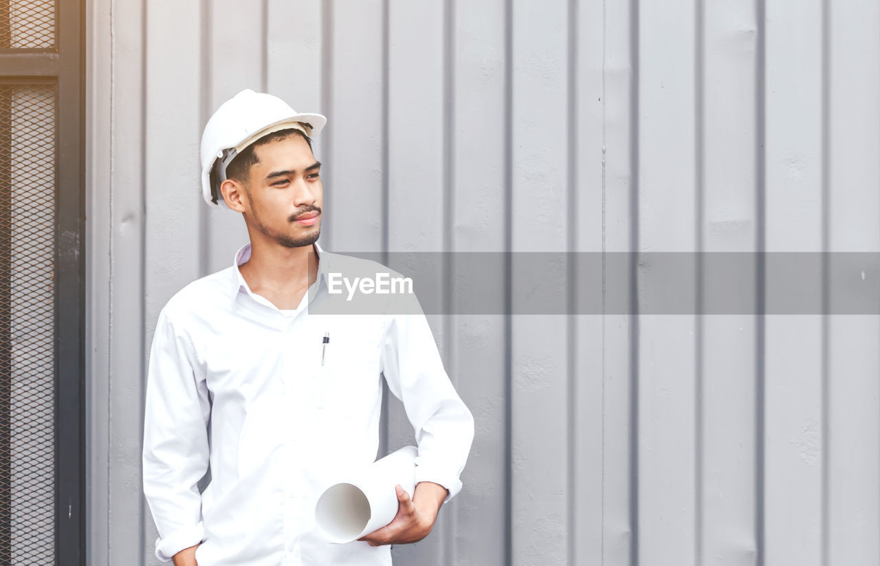 Engineer wearing hardhat holding blueprint outdoors