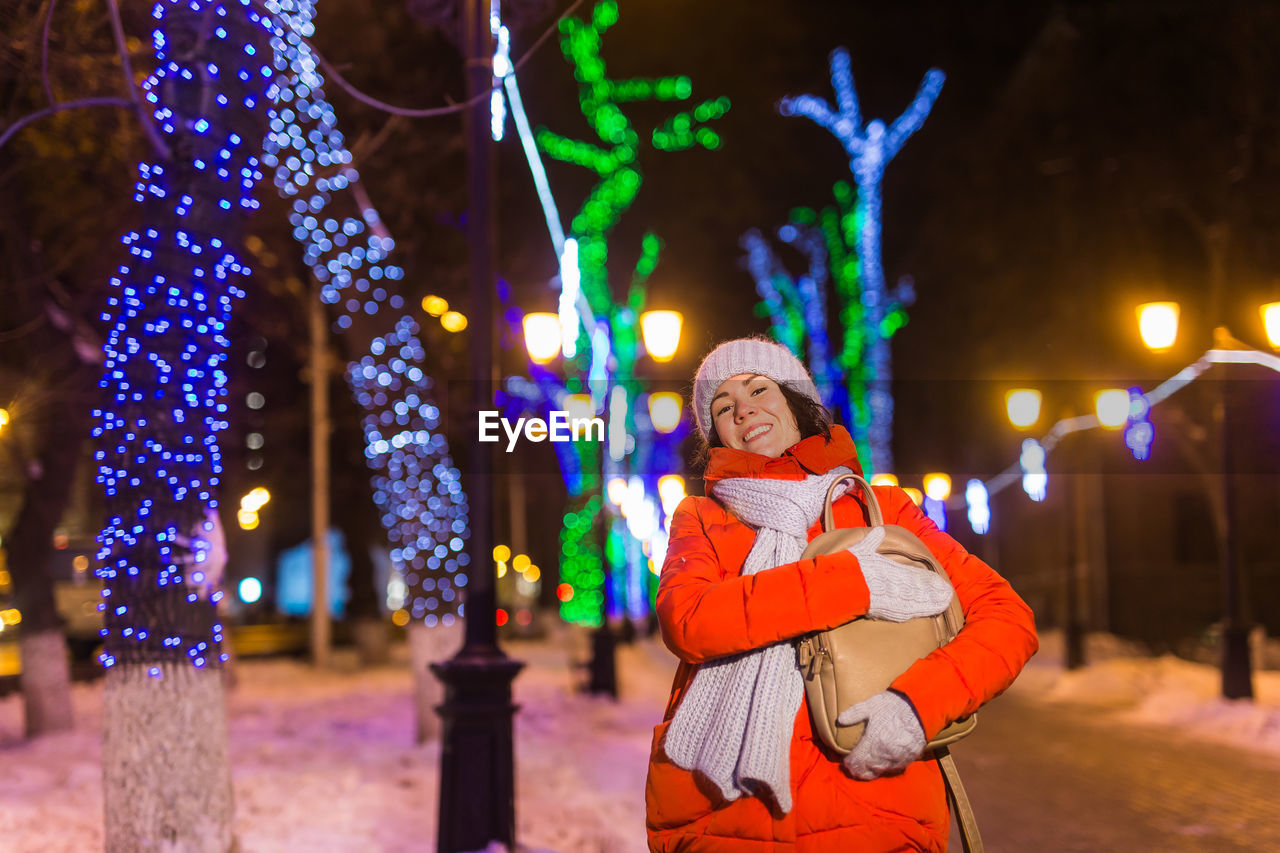 PORTRAIT OF WOMAN STANDING IN ILLUMINATED CITY