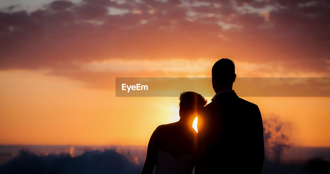 Silhouette couple standing at beach against sky during sunset