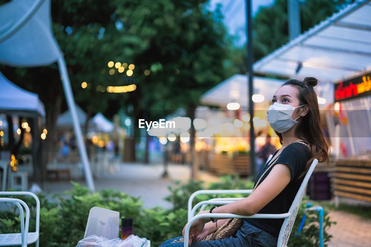 Young women wearing surgical mask sitting in relax zone of night market , chiang mai thailand