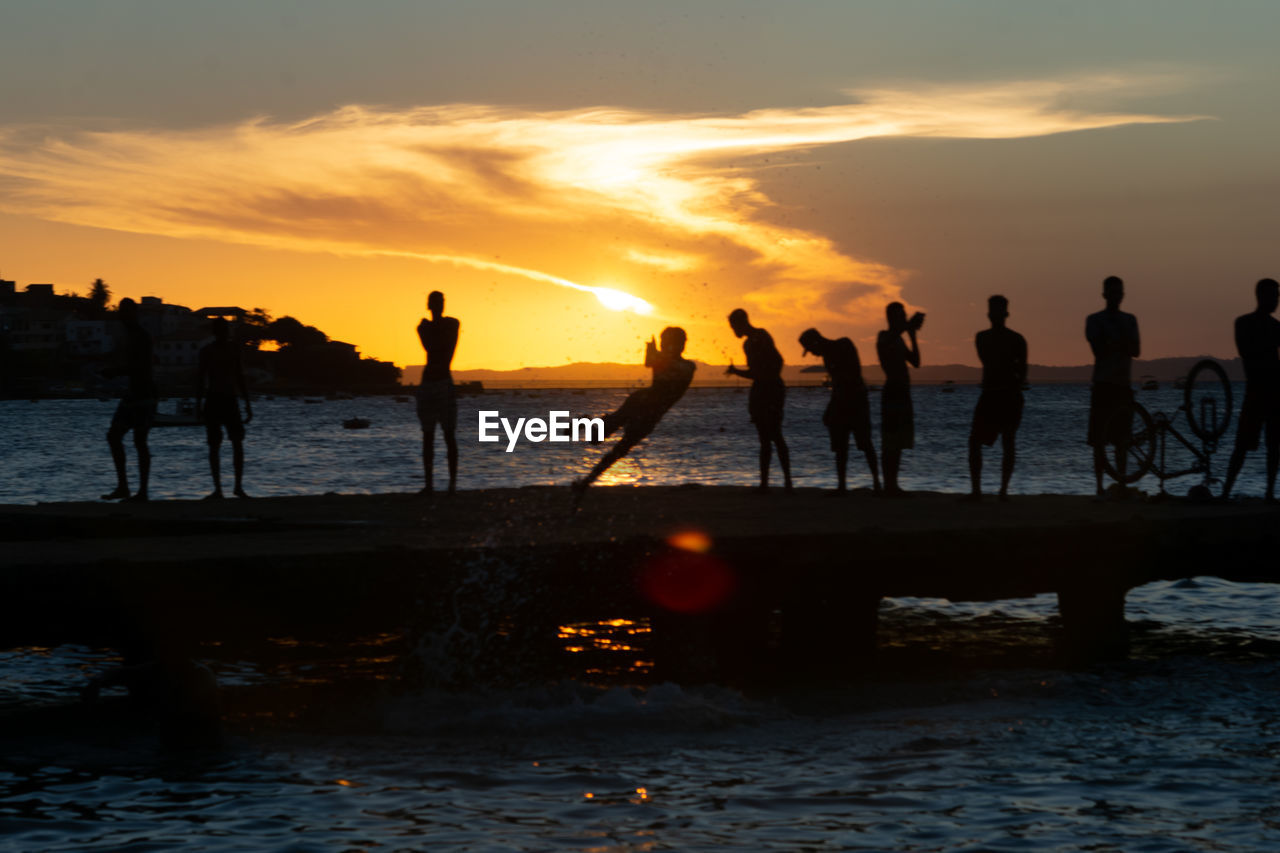  dozens of young people, in silhouette, are seen on top of the crush bridge having fun. 