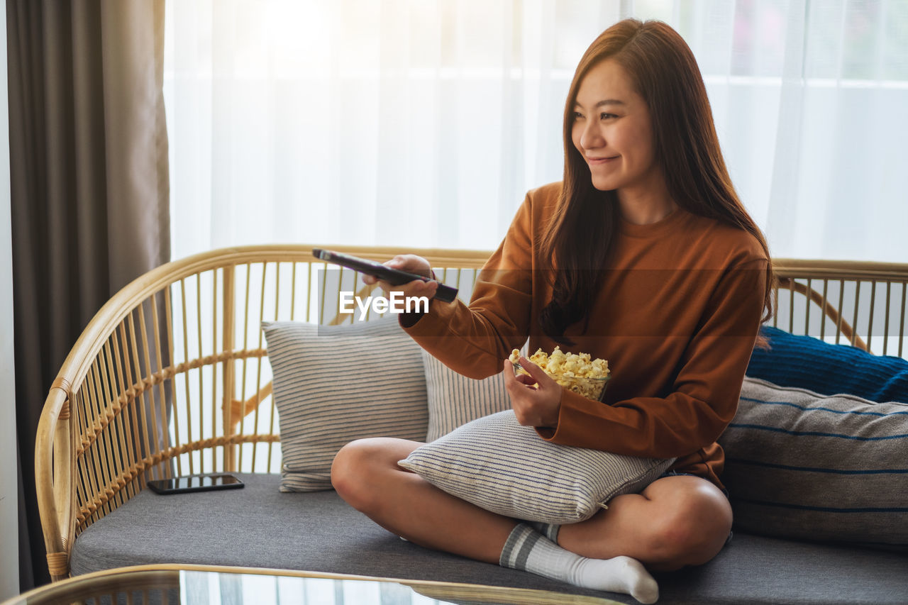 young woman using mobile phone while sitting on chair at home