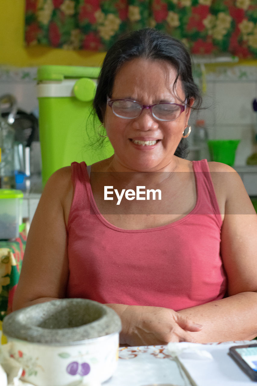 Smiling mature woman with eyes closed sitting by table at home