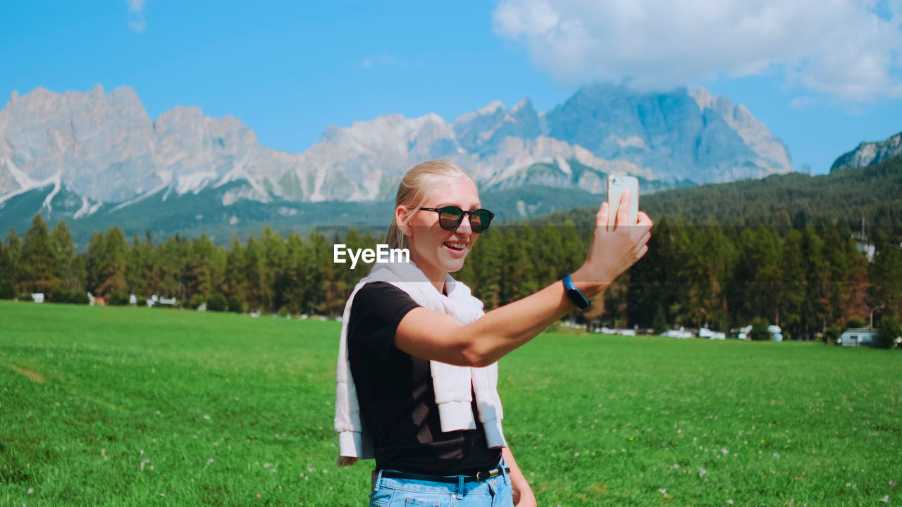 full length of young man with arms outstretched standing on field against mountain