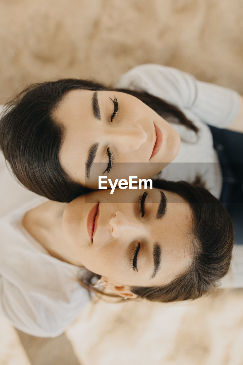 Young female twins with eyes closed on sand