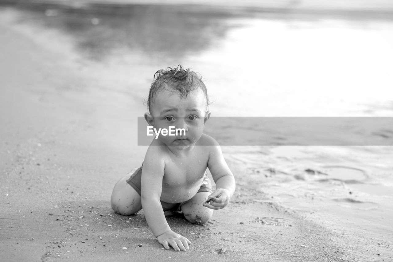 Portrait of cute shirtless baby boy crawling on shore at beach