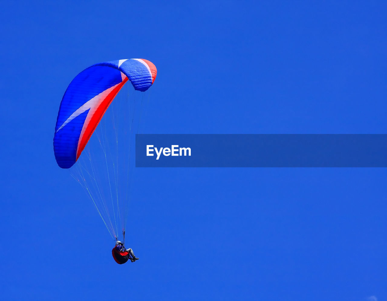 Low angle view of person paragliding against clear blue sky 