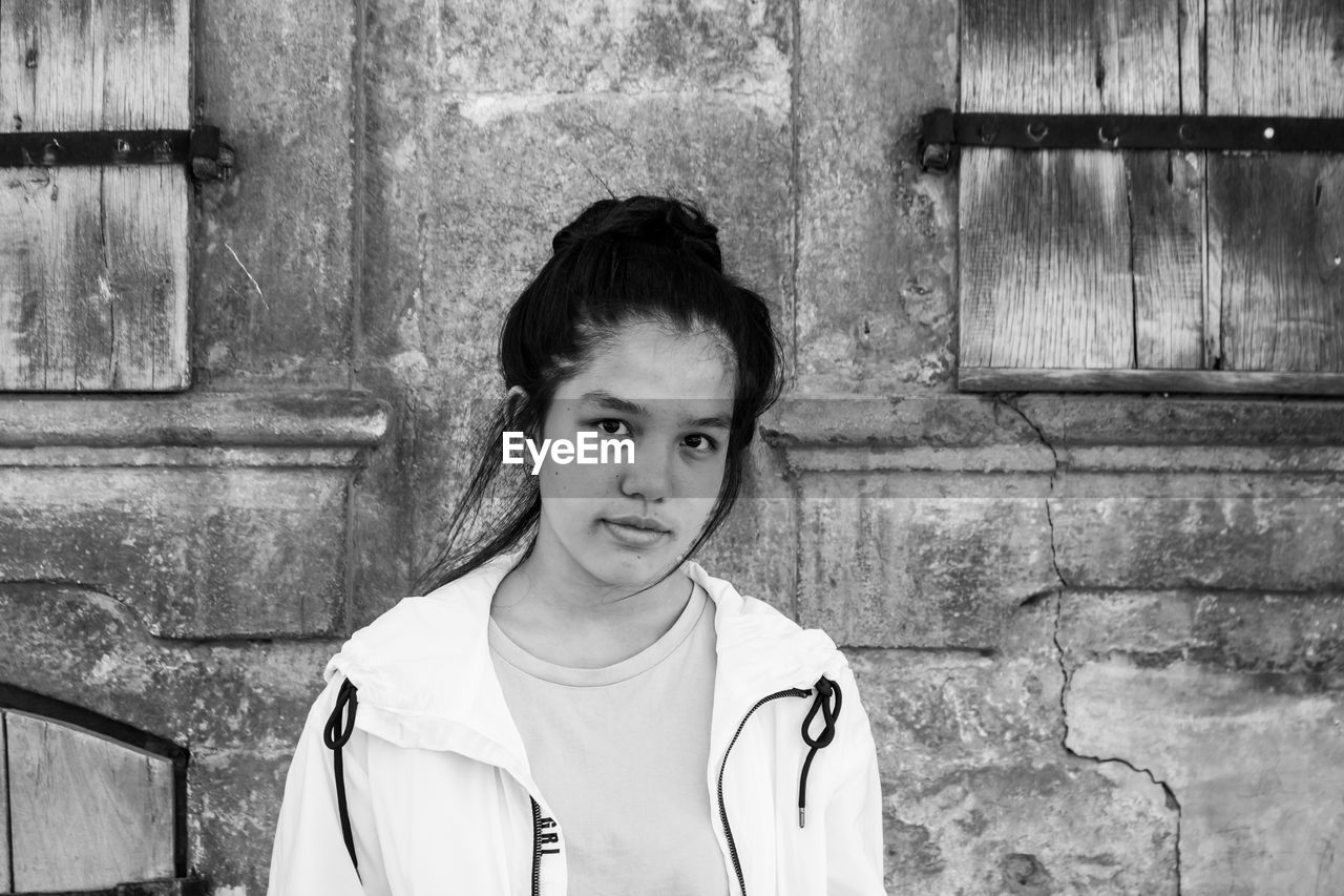 Portrait of young woman against weathered wall