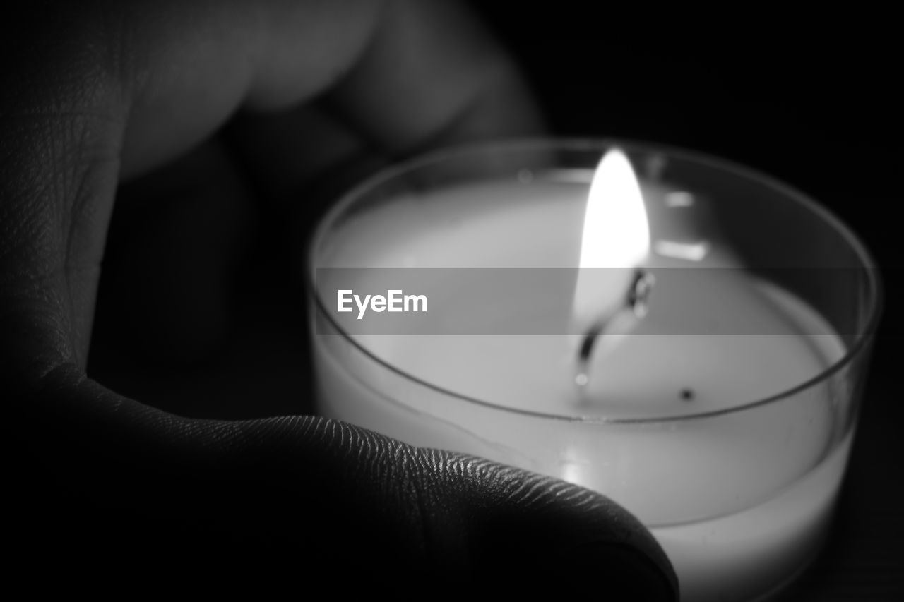 Cropped hand holding lit candle against black background