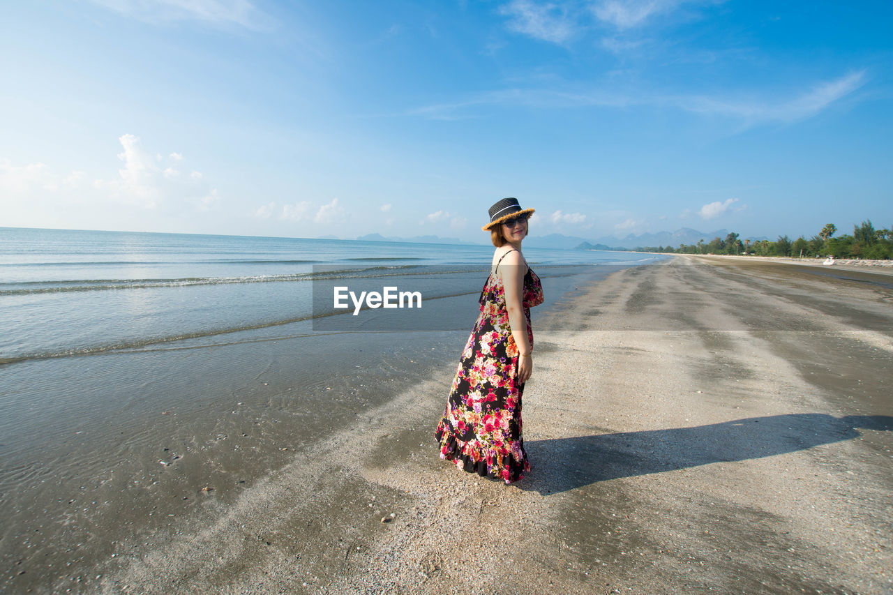 Side view of woman standing on sand at beach against sky