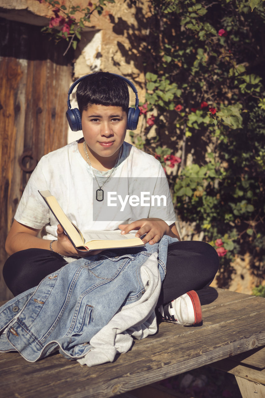one person, sitting, full length, child, men, person, spring, casual clothing, childhood, clothing, leisure activity, front view, portrait, lifestyles, wood, nature, looking at camera, day, relaxation, outdoors, adult, music, footwear, plant, young adult, photo shoot, tree, activity, publication