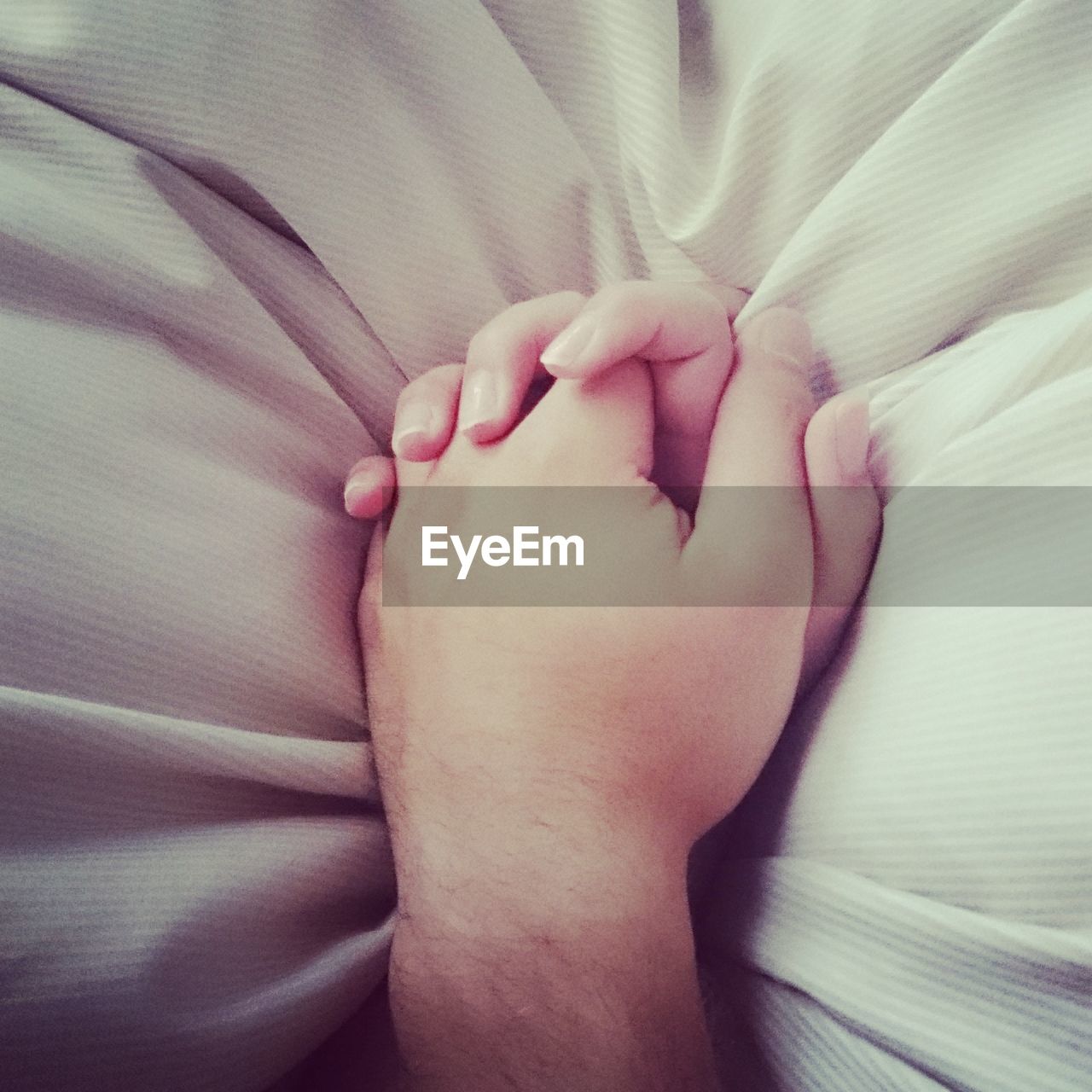 Cropped hands of couple on bed at home