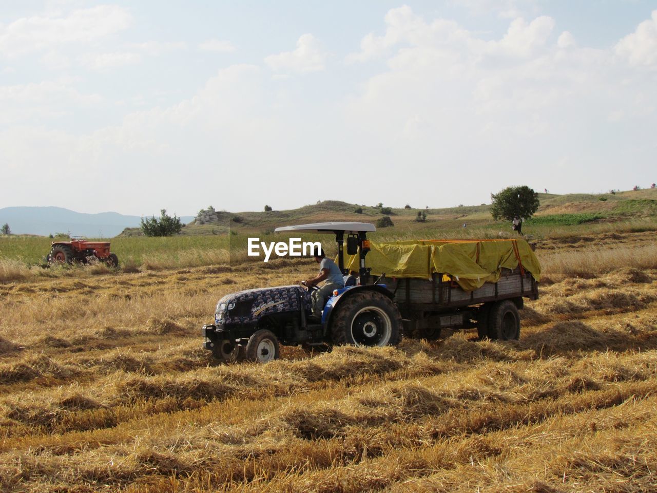 Farmer with agricultural machinery on field against sky