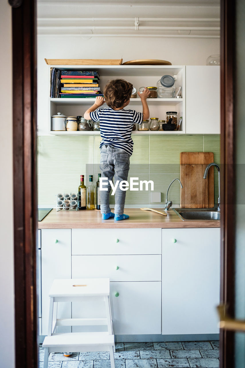 Rear view of boy standing on kitchen counter at home