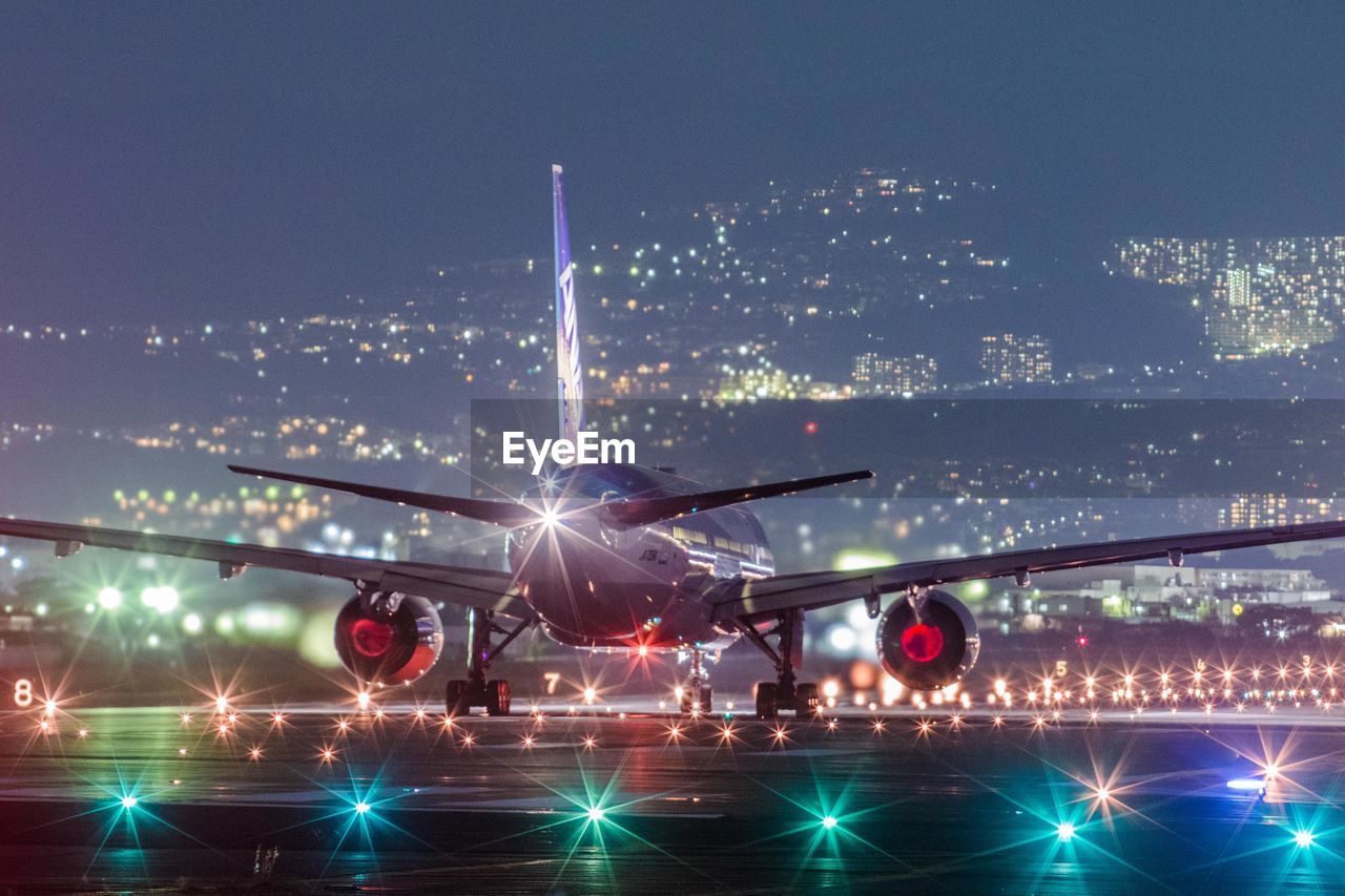 Airplane flying over illuminated airport runway against clear sky at night