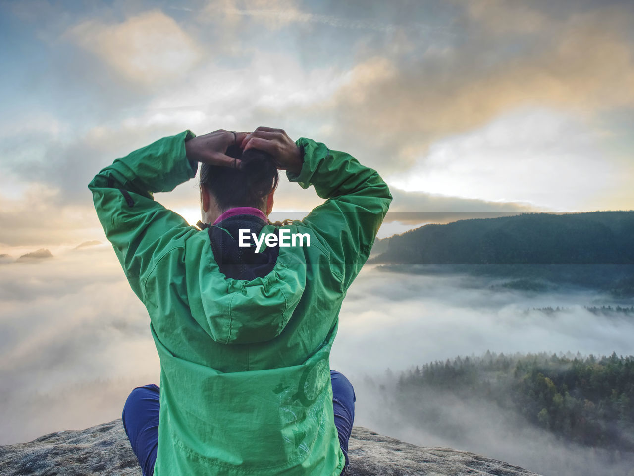 Woman sit on cliff edge and looking to rising sun above misty valley. foggy mountain. man hike