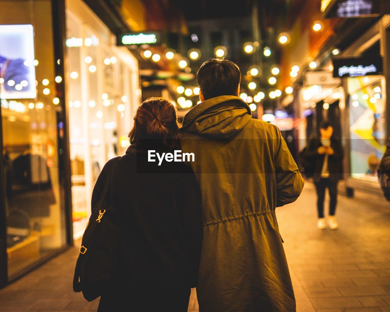 REAR VIEW OF COUPLE STANDING ON ILLUMINATED STREET