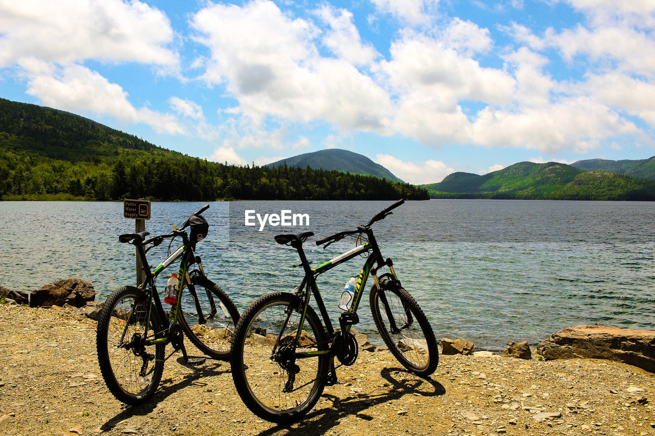 Bicycles by river against cloudy sky on sunny day