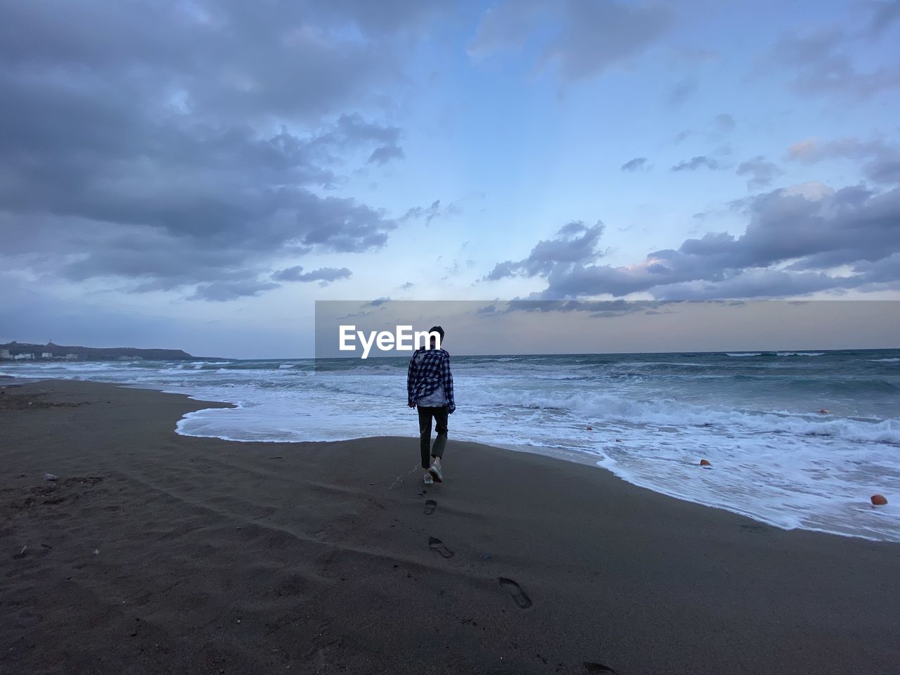 Rear view of man walking at beach against sky