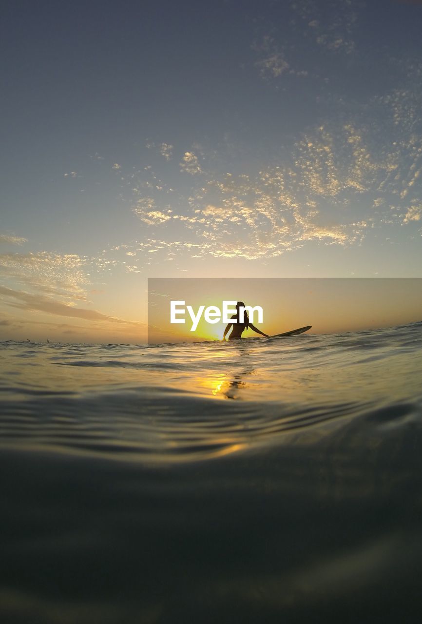 Surface level view of woman surfing on sea against sky during sunset