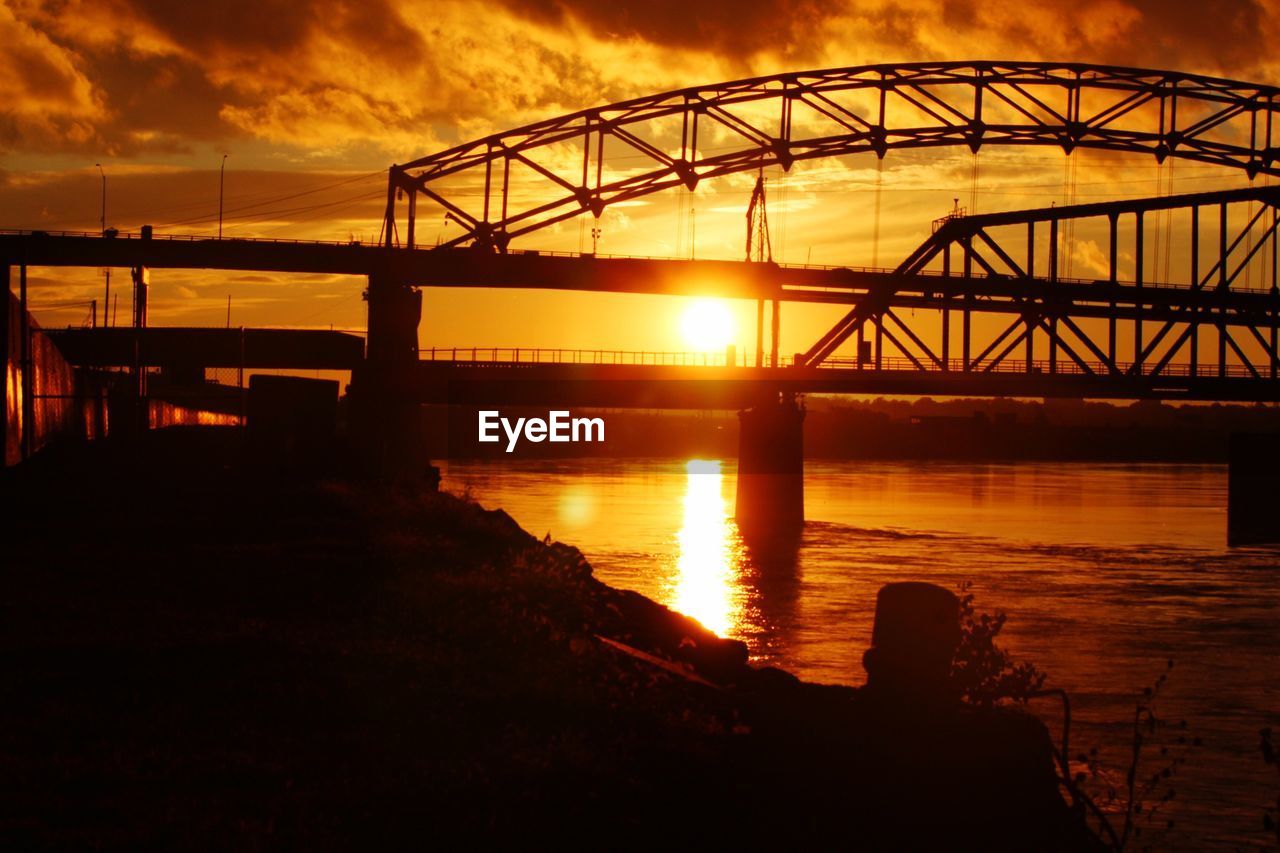 Silhouette bridge over river against sky during sunset