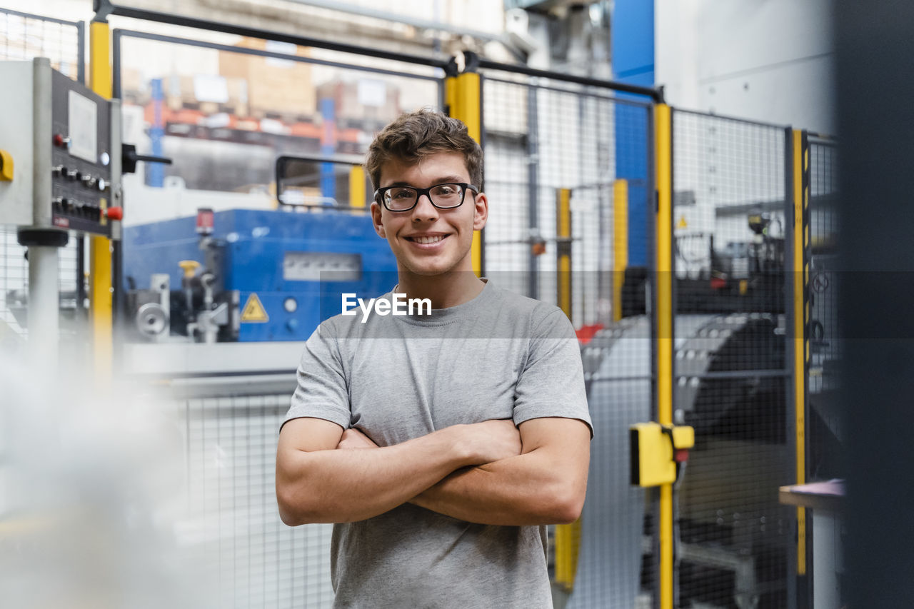 Smiling male engineer with arms crossed standing in illuminated industry