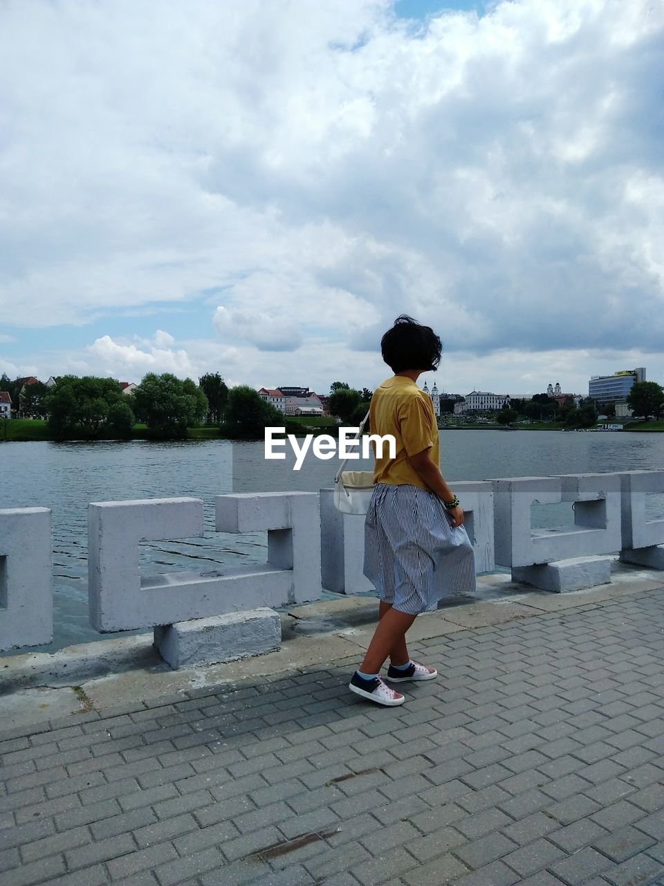 FULL LENGTH REAR VIEW OF BOY STANDING ON SHORE AGAINST SKY