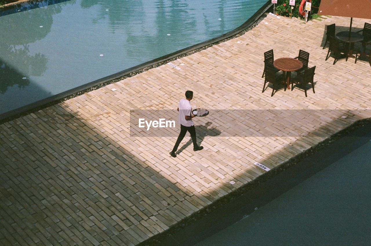 HIGH ANGLE VIEW OF WOMAN SWIMMING IN POOL AT RESORT