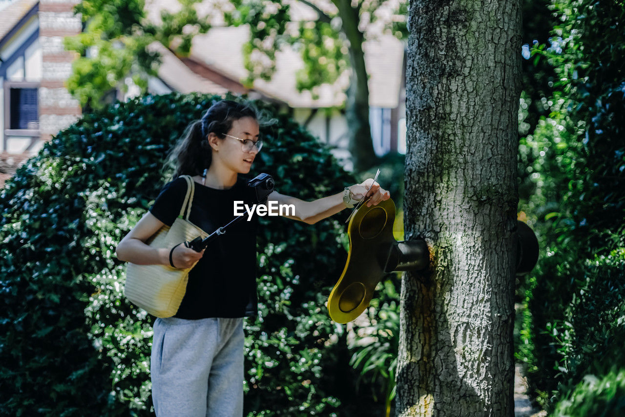 Portrait of teenage with a camera on a stick turns a large golden key sticking out of a tree trunk